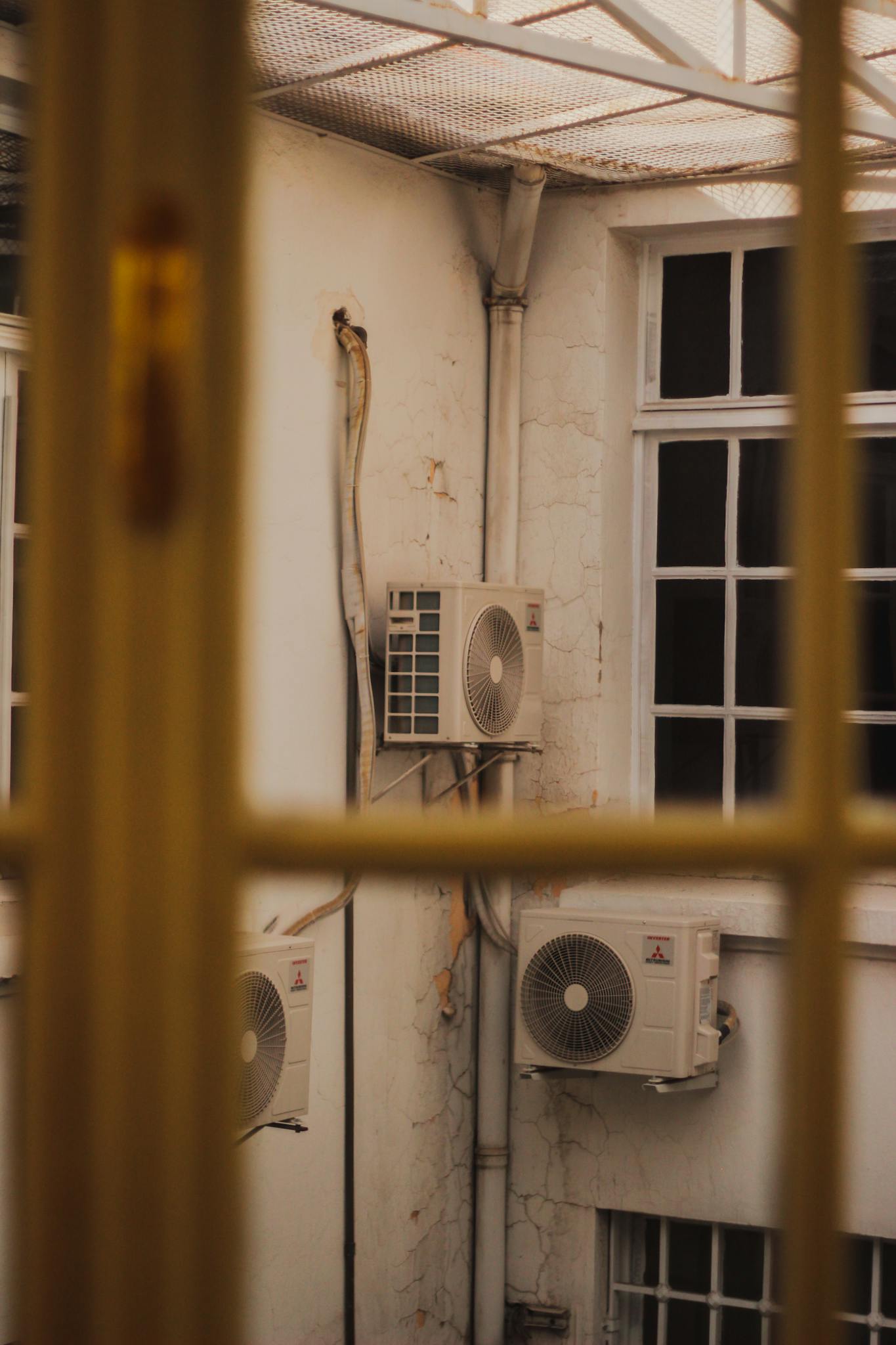 Air conditioners attached to the exterior of an old building, seen through a window.