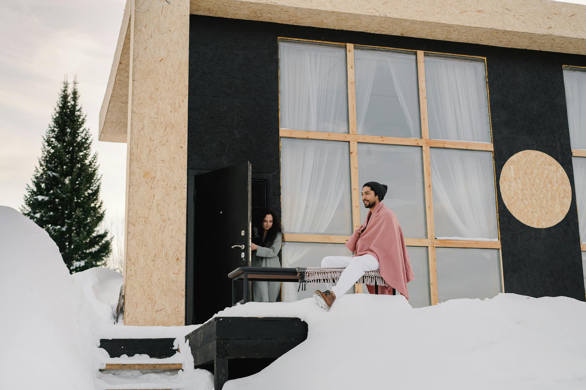Contemporary house in a snowy setting with two people enjoying a winter day.